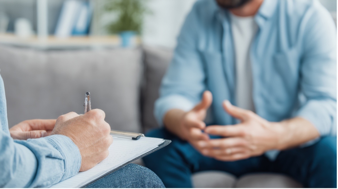 Therapist takes notes on a clipboard while client explains things in a therapy session.