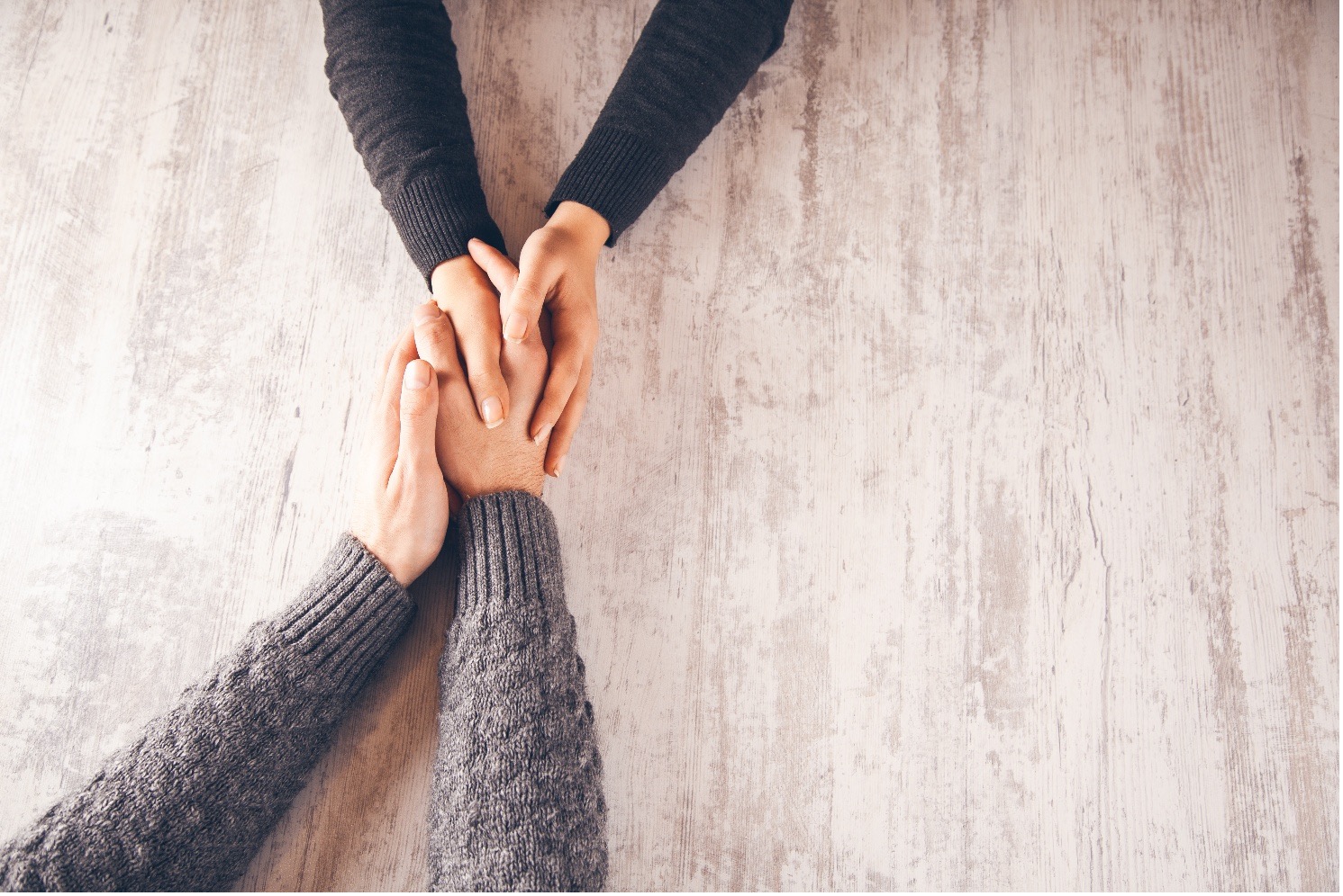 Why Couples Seek Relationship Counselling - Clear Day Consulting, Counselling & Coaching Several hands stacked over one another on a light wooden table, symbolizing teamwork and support.